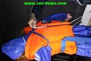 Stella helps Ronja to pullover a lifevest the other way round both wearing shiny nylon downwear (Pics)