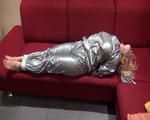 Sophie tied and gagged on the sofa wearing a shiny silver PVC sauna suit (Video)