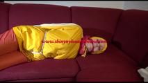 Lucy tied, gagged and hooded on a red sofa wearing a sexy orange shiny nylon pants and a yellow rain jacket (Video)