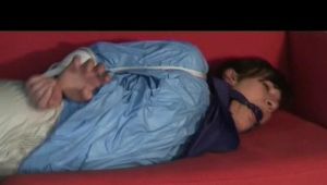 Julia tied and gagged on a sofa wearing a shiny light blue/beige PVC suit (Video)