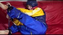 Sonja ties, gagges and hoodes herself on a sofa with a bar and a ball gag wearing a sexy blue shiny nylon rain pants and a yellow rain acket and a blue down jacket (Video)