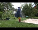 Jill wearing a shiny yellow rainpants and rain jacket pulls over a raincoat and playing with water our of the water hose (Video)