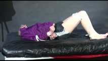 Pia tied and gagged with belts on a bed wearing a sexy black shiny nylon shorts and a purple rain jacket (Video)