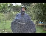 Jill wearing a shiny yellow rainpants and rain jacket pulls over a raincoat and playing with water our of the water hose (Video)