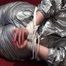 Sophie tied and gagged on the sofa wearing a shiny silver PVC sauna suit (Video)