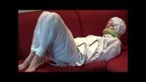 Pia tied and gagged on a sofa wearing a shiny white rainsuit (Video)