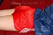 Lucy wearing a sexy red shiny nylon shorts and a blue shiny nylon rain jacket during reading a bit on the sofa (Pics)
