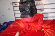 Sonja tied and gagged with a pillory on bed wearing a sexy red rain pants and a black down jacket (Pics)