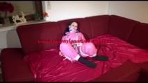 Lucy tied and gagged with ropes on a sofa wearing a pink oldschool shiny nylon down skibib freeing herself at the end (Video)
