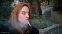 Absolutely stunning lady is smoking two long cigarettes in the park