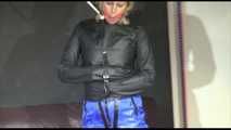 PIA wearing a straight jacket over a shiny nylon rain jacket and a rain pants as well as a neckband tied overhead and a ball gag (Video)