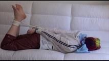 Mara tied and gagged on a white sofa in a reading lounge wearing a sexy brown rain pants and a white rain jacket (Video)