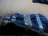 One of our archive girl tied, hooded and gagged by tape on a bed wearing shiny nylon rainwear (Video)