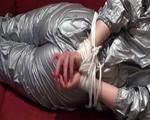 Sophie tied and gagged on the sofa wearing a shiny silver PVC sauna suit (Video)