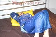 Lucy putting on an blue agu rain pants and rain jacket and lolling on bed in shiny nylon bed cloths (Pics)