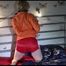 Sonja wearing a sexy super small red shiny nylon shorts and an orange rain jacket tied on bed with neckband and cuffs, gagged with a ball in a cloth (Video)
