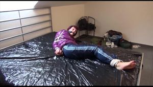 Mara tied and gagged on bed wearing s shiny purple down jacket and blue rain pants (Video)