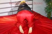 Sonja tied and gagged with a pillory on bed wearing a sexy red rain pants and a black down jacket (Pics)