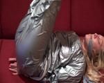 Sophie tied and gagged on the sofa wearing a shiny silver PVC sauna suit (Video)