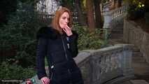 Absolutely stunning lady is smoking two long cigarettes in the park