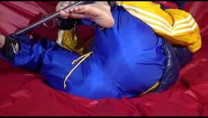 Sonja ties, gagges and hoodes herself on a sofa with a bar and a ball gag wearing a sexy blue shiny nylon rain pants and a yellow rain acket and a blue down jacket (Video)