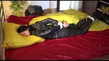 Lucy tied and gagged on bed wearing a sexy black shiny nylon pants and a black rain jacket (Video)