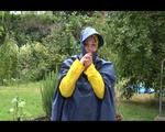 Jill wearing a shiny yellow rainpants and rain jacket pulls over a raincoat and playing with water our of the water hose (Video)