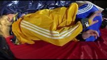 Sonja tied and gagged with a bar and cuffs in bed wearing a very small, hot blue shiny nylon shorts and a yellow rain jacket (Video)