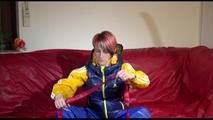 Sonja ties, gagges and hoodes herself on a sofa with a bar and a ball gag wearing a sexy blue shiny nylon rain pants and a yellow rain acket and a blue down jacket (Video)