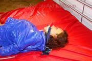 Lulu tied and gagged on a bed wearing a blue shiny nylon shorts and a blue rainjacket (Pics)