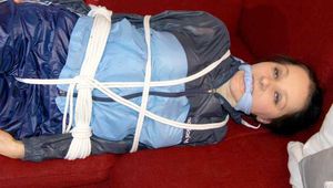 Lucy wearing a blue shiny nylon pants and an oldschool blue rain jacket tied and gagged with ropes on a sofa (Pics)